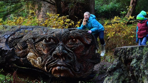 Children exploring the tree sculpture known as Douglas, carved on a fallen fir at Cragside, Northumberland